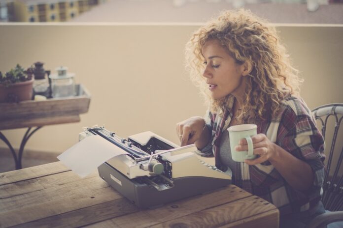 Beautiful writer woman with old typewriter working - concept of alternative technology and work - pretty people with different lifestyle enjoying life
